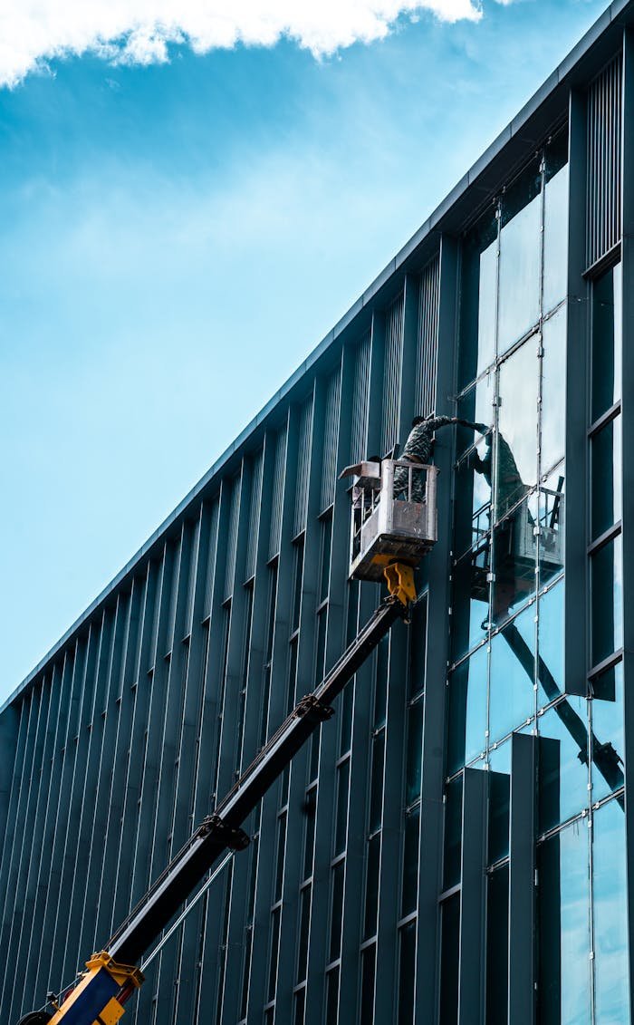 Person on crane cleaning skyscraper windows under blue sky.